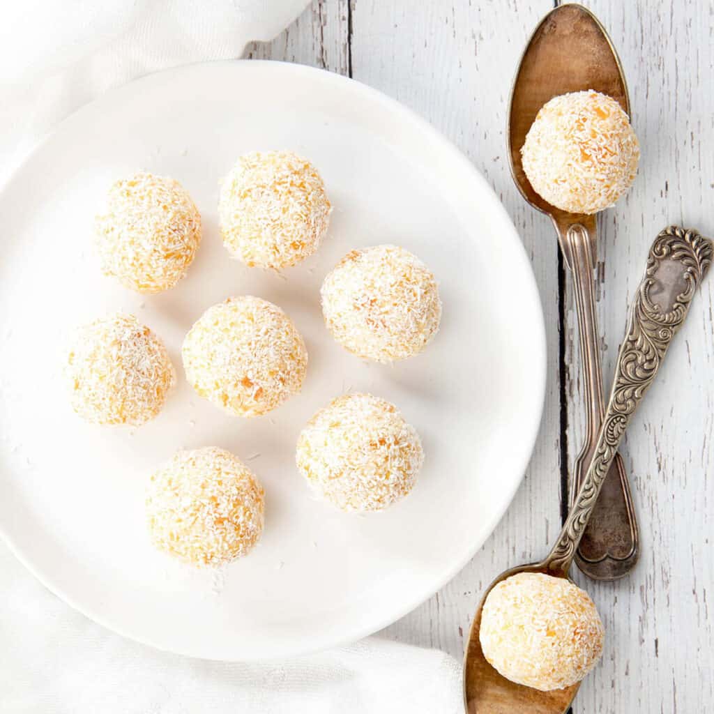 Apricot Bliss Balls on a white background and White Plate with decorative spoons